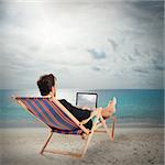 Man on deckchair with laptop at beach