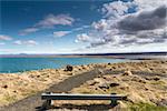 Horizontal panorama of a wooden resting bench with a beautiful shoreline in the background and dramatic clouds above