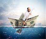 Businessman paddling on a big banknote boat