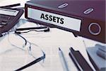 Assets - Office Folder on Background of Working Table with Stationery, Glasses, Reports. Business Concept on Blurred Background. Toned Image.