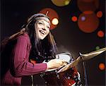 1970s SMILING YOUNG WOMAN WEARING HEADBAND PLAYING DRUMS