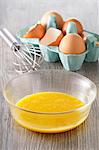Egg yolks in a bowl, eggs in an egg box and a whisk