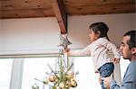 Father lifting toddler girl putting star on Christmas tree