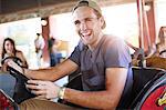 Laughing young man riding bumper cars at amusement park