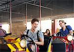 Laughing young men riding bumper cars at amusement park