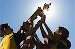 A group of boys in soccer team shirts holding a trophy and celebrating a win.