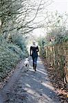 A woman walking with a dog on a country lane.