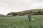 A woman walking with a dog across a grass field.
