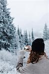 A woman using a smart phone, photographing pine forests in snow,