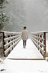 A woman walking on a footbridge in the mountains in snow.