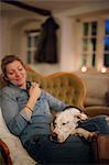 A woman seated on a sofa with a large dog with his head on her lap.