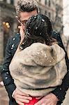 A couple, lovers kissing in lightly falling snow in the city.