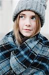 A young girl in a tartan plaid shawl and woolly hat outdoors in the winter.