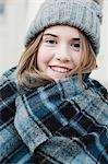 A young girl in a tartan plaid shawl and woolly hat outdoors in the winter.