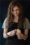 A woman in a blue apron peeling an apple with a knife.