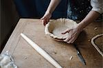 A woman working smoothing the edge of a pastry case lining a pie dish.