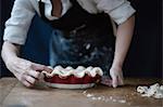 A woman in a kitchen decorating the pastry top of a home made pie.