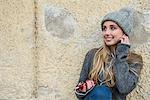 Teenage girl listening to music on mobile phone and leaning against wall, Munich, Bavaria, Germany