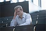 Young man sitting with tension in lecture hall with head in hands, Freiburg im Breisgau, Baden-Württemberg, Germany