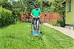 Boy cutting grass around the house in summertime - focusing on the operation