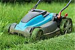 Blue lawnmower cutting grass, with fresh cut strip in the foreground - closeup