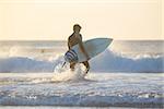 Male surfer on the beach with the surfboard in sunset.  Vertical composition.