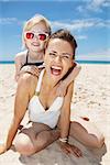 Family fun on white sand. Portrait of smiling mother and daughter in swimsuits at sandy beach on a sunny day