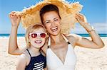 Family fun on white sand. Portrait of smiling mother and daughter under big straw hat at sandy beach on a sunny day