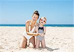 Family fun on white sand. Happy mother and child in swimsuits at beach on a sunny day showing hands full of sand