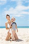 Family fun on white sand. Smiling mother and child in swimsuits at sandy beach on a sunny day