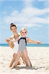 Family fun on white sand. Smiling mother and child in swimsuits playing at sandy beach on a sunny day