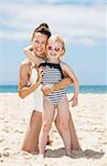 Family fun on white sand. Portrait of happy mother and child in swimsuits hugging at sandy beach on a sunny day