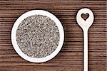 Chia seeds on white porcelain plate with cooking wooden spoon (cut heart shape) on wood background table.