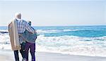 Senior couple standing on beach, looking at ocean, rear view