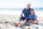 Portrait of grandfather and grandson, sitting on beach, smiling