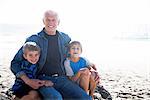 Grandfather with two grandsons, sitting on beach, smiling