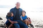 Grandfather with two grandsons, sitting on beach, smiling