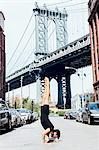 Young man doing yoga handstand in front of Manhattan Bridge, New York, USA
