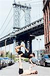 Man balancing on top of another in yoga position by Manhattan Bridge, New York, USA