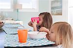 Side view of sisters at dining table eating breakfast