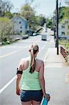 Rear view of woman wearing activity tracker carrying water bottle walking along road