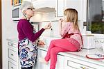 Senior woman and granddaughter eating popcorn at kitchen counter