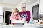 Girl and grandmother preparing greaseproof paper at kitchen counter