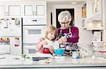 Girl and grandmother pouring cake mix at kitchen counter