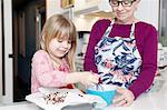 Girl whisking cake at kitchen counter with grandmother