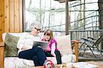 Senior woman and granddaughter browsing digital tablet on living room sofa