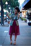 Woman standing in street, holding smartphone, wearing earphones, smiling