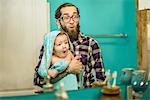 Mirror image of young man and baby son pulling faces in bathroom