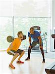 Personal trainer guiding man doing barbell squats at gym