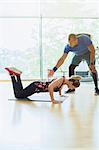 Personal trainer guiding woman doing push-ups on knees at gym